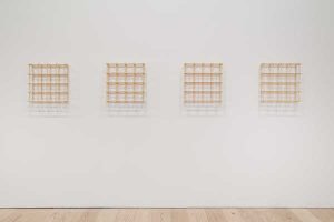 Four identical wood grids line a white gallery wall