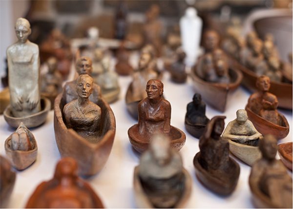 Small, terra-cotta boats carry people of various ages with different facial expressions.